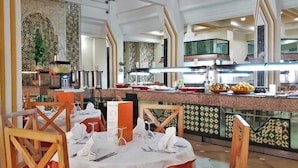 A restaurant with a buffet setup, tables with white tablecloths, and a tiled backsplash. - Sun Palm  (douz)