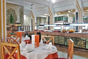 Ein Restaurant mit einem Buffet, Tischen mit weißen Tischdecken und einer gefliesten Rückwand.
