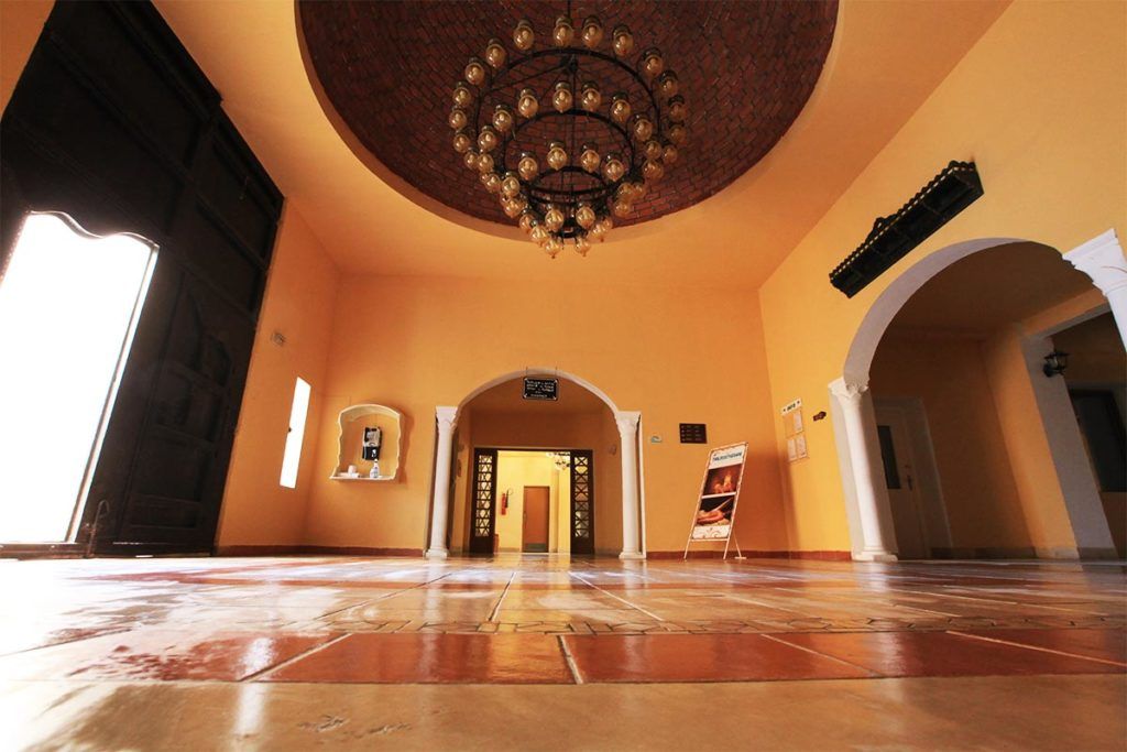 Um hall amplo com teto alto, um candelabro e uma grande porta aberta para outra área.