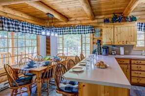 Ein Holzblock-Innenraum mit Essbereich, Küche und großen Fenstern.