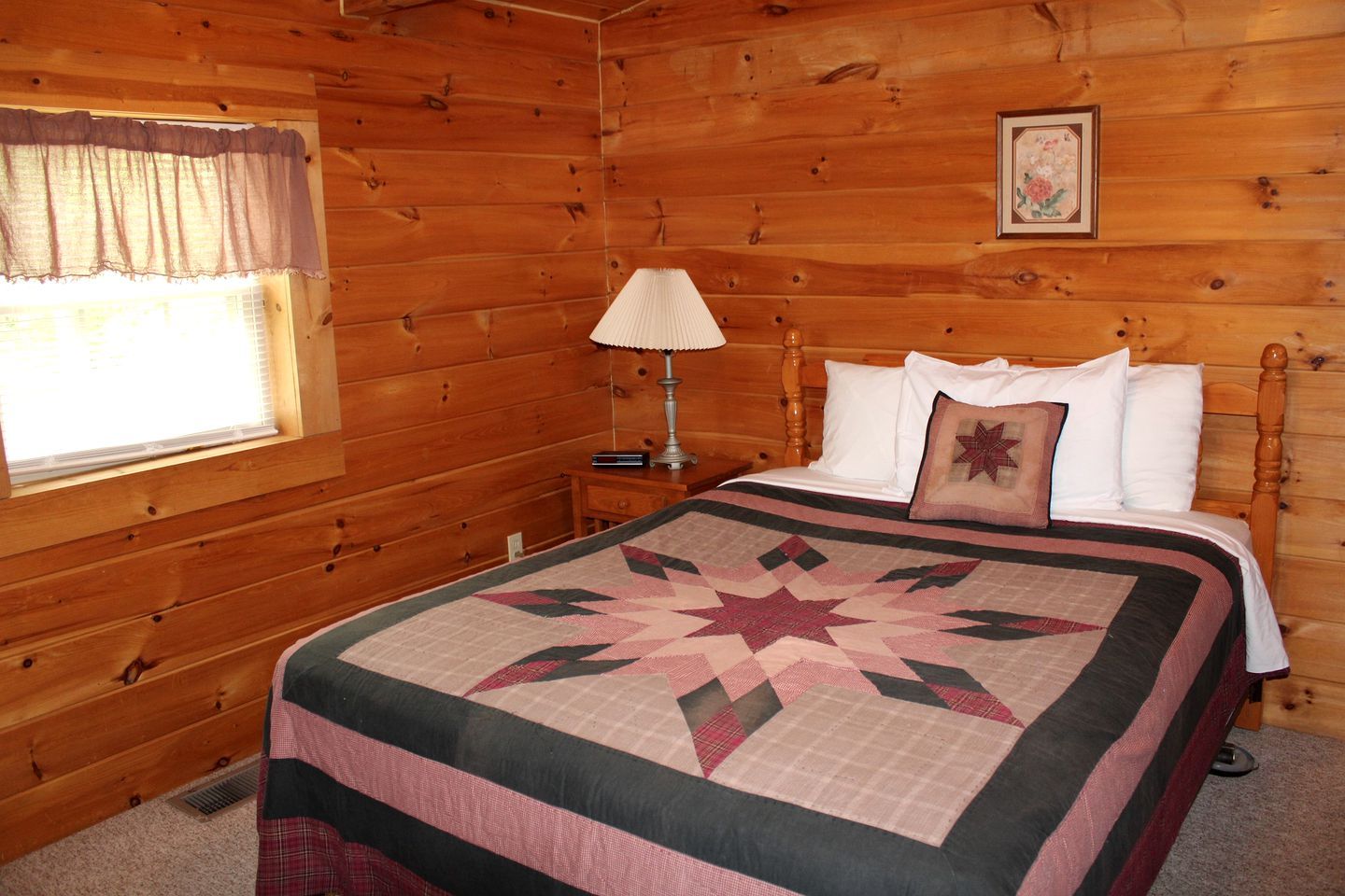 Une chambre à coucher dans une cabane en bois, avec un lit, une table de chevet, une lampe et une fenêtre avec des rideaux.