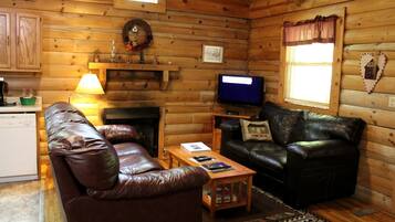 A cozy cabin interior with a fireplace, leather sofas, a television, and a small table.