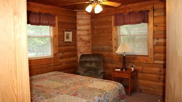 A log cabin bedroom with a bed, a chair, a lamp, and a ceiling fan.