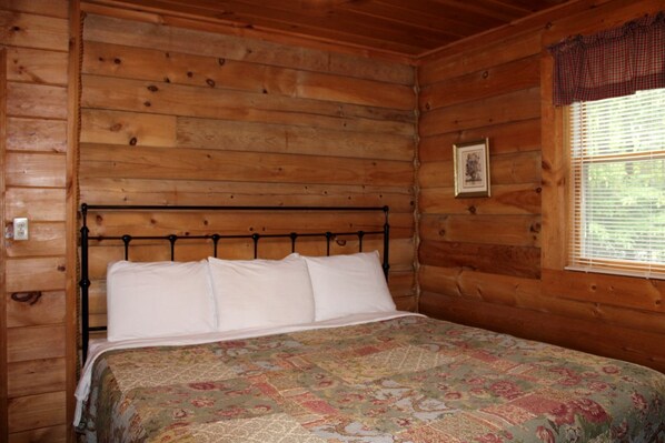 A wooden cabin room with a bed, a window with blinds, and a framed picture on the wall. - Charming Cabin Rental in the Forest near Beckley, West Virginia (Hico)