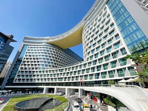 A modern hotel with a curved facade, multiple floors, and a central courtyard with a fountain. - Luxury One-Bedroom Seven Palm | Beach & Pool (Dubai)