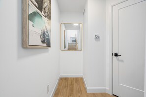 Ein Flur mit Holzboden, einer weißen Tür und einem gerahmten Kunstwerk an der Wand.