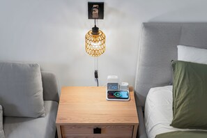 Ein Hotelzimmer mit einem Nachttisch aus Holz, einer digitalen Uhr, einer Steckdose und einer Wandlampe.