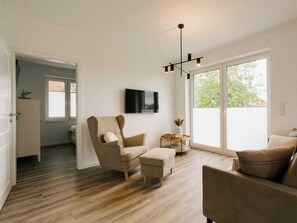 Una sala de estar moderna con sofá, sillón y reposapiés, un televisor de pantalla plana y una lámpara colgante.