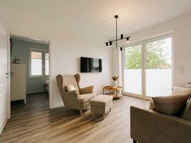 A modern living room with a sofa, armchair, and ottoman, a flat-screen TV, and a pendant light.