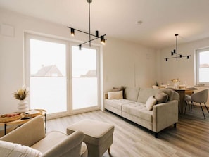 Uma sala de estar moderna com um sofá, um banquinho e uma área de jantar com uma mesa e cadeiras.