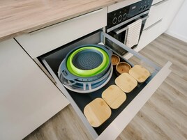 Un cajón de cocina con un colador, cuencos y tablas de cortar de madera.