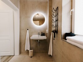Un baño con lavamanos, espejo, toallero y un pequeño cubo de basura.
