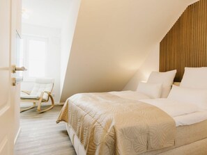 A bedroom with a bed, a chair, and a wooden slatted headboard. - Holiday Apartment in Greetsiel With Balcony (Krummhoern)
