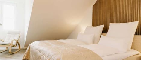 Un dormitorio con cama, almohadas, cabecera de madera y una mecedora.