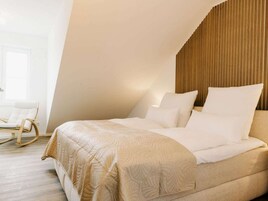 Un dormitorio con cama, almohadas, cabecera de madera y una mecedora.