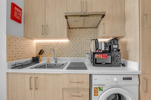 Eine kompakte Küche mit Spüle, Kaffeemaschine, Toaster und Waschmaschine.