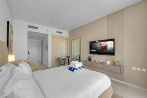Ein Hotelzimmer mit einem Bett, einem an der Wand befestigten Fernseher, einem Schreibtisch mit Stuhl und einem Spiegel.