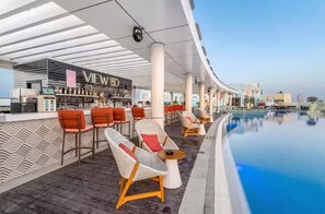 A bar area with a view of the pool and outdoor seating. - Seven Palm Luxury Studio | Beach & Rooftop Pool (Dubai)