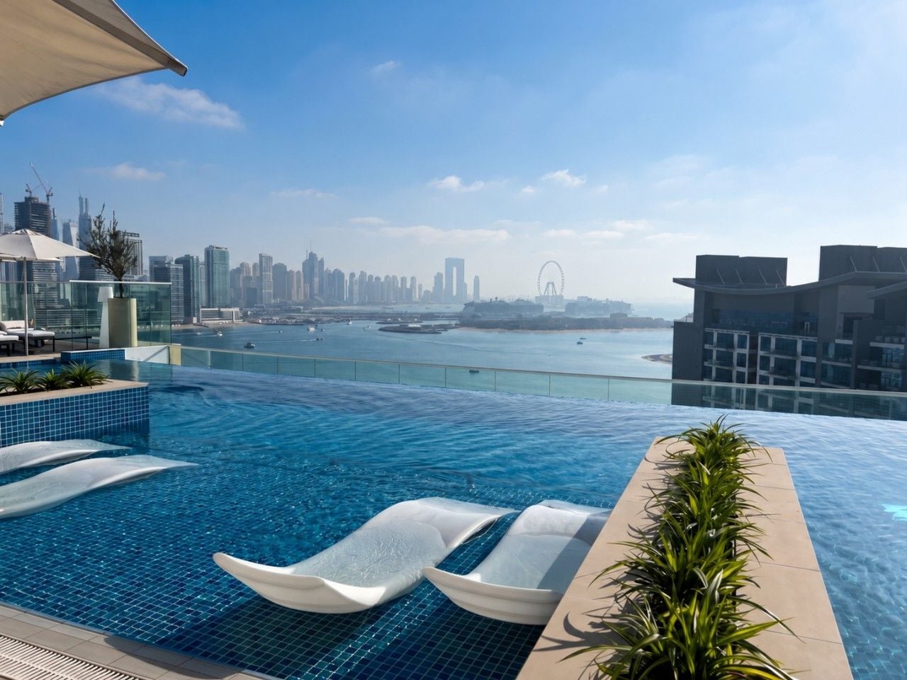 A rooftop infinity pool with lounge chairs, a view of a city skyline, and a body of water.