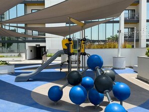 An outdoor play area with a slide, climbing structure, and exercise balls. - Sunlit High-Floor 1BR | Sobha The Crest Tower B (Dubai)