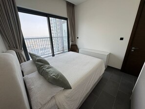 A hotel room with a large bed, a sofa, a window with curtains, and a view of a cityscape. - Sunlit High-Floor 1BR | Sobha The Crest Tower B (Dubai)