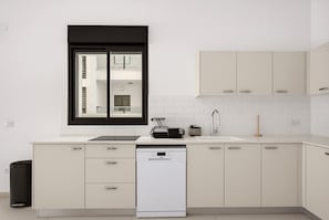 Eine moderne Küche mit weißen Schränken, einem Fenster mit schwarzem Rahmen, einem eingebauten Geschirrspüler und einer Spüle aus Edelstahl.