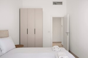Ein Schlafzimmer mit Bett, Kleiderschrank und einem durchgehenden Türbogen sichtbarem Badezimmer.