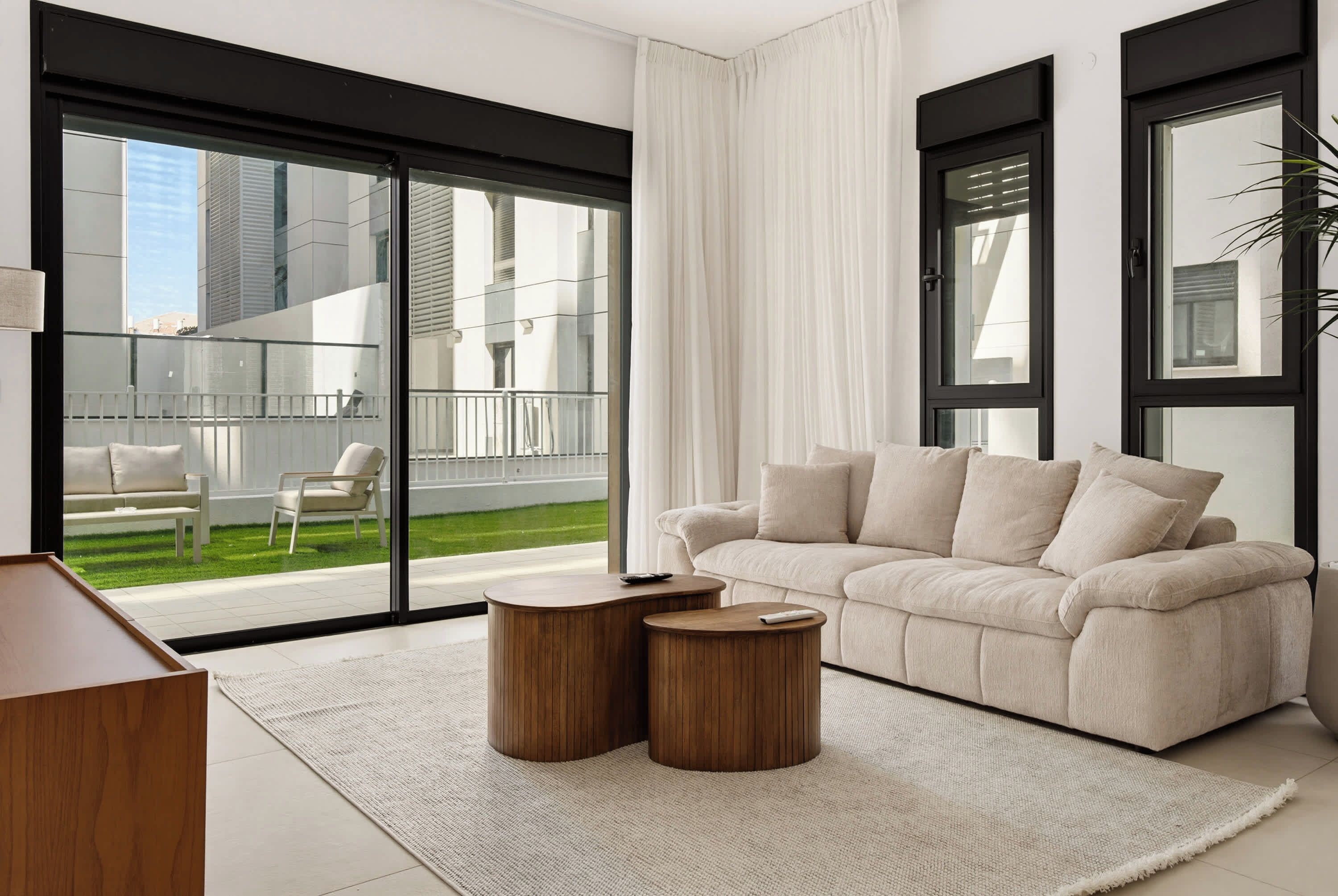 A modern living room with a sofa, two wooden side tables, and a view of a balcony.