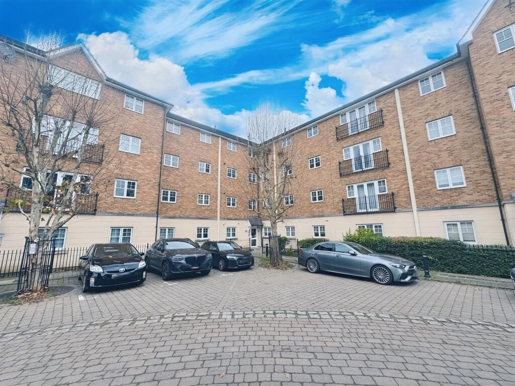 Un edificio residencial de varios pisos con fachada de ladrillo, un patio empedrado y varios coches estacionados.