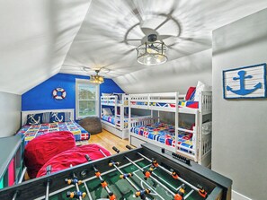 A room with bunk beds, a foosball table, and a ceiling fan. - Luxury Beach House | Private Heated Pool, Lagoon Views & Games | Walk to Beach (Hilton Head Island)