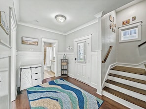 A hallway with a wooden staircase, white doors, a patterned rug, and a ceiling light fixture. - Luxury Beach House | Private Heated Pool, Lagoon Views & Games | Walk to Beach (Hilton Head Island)