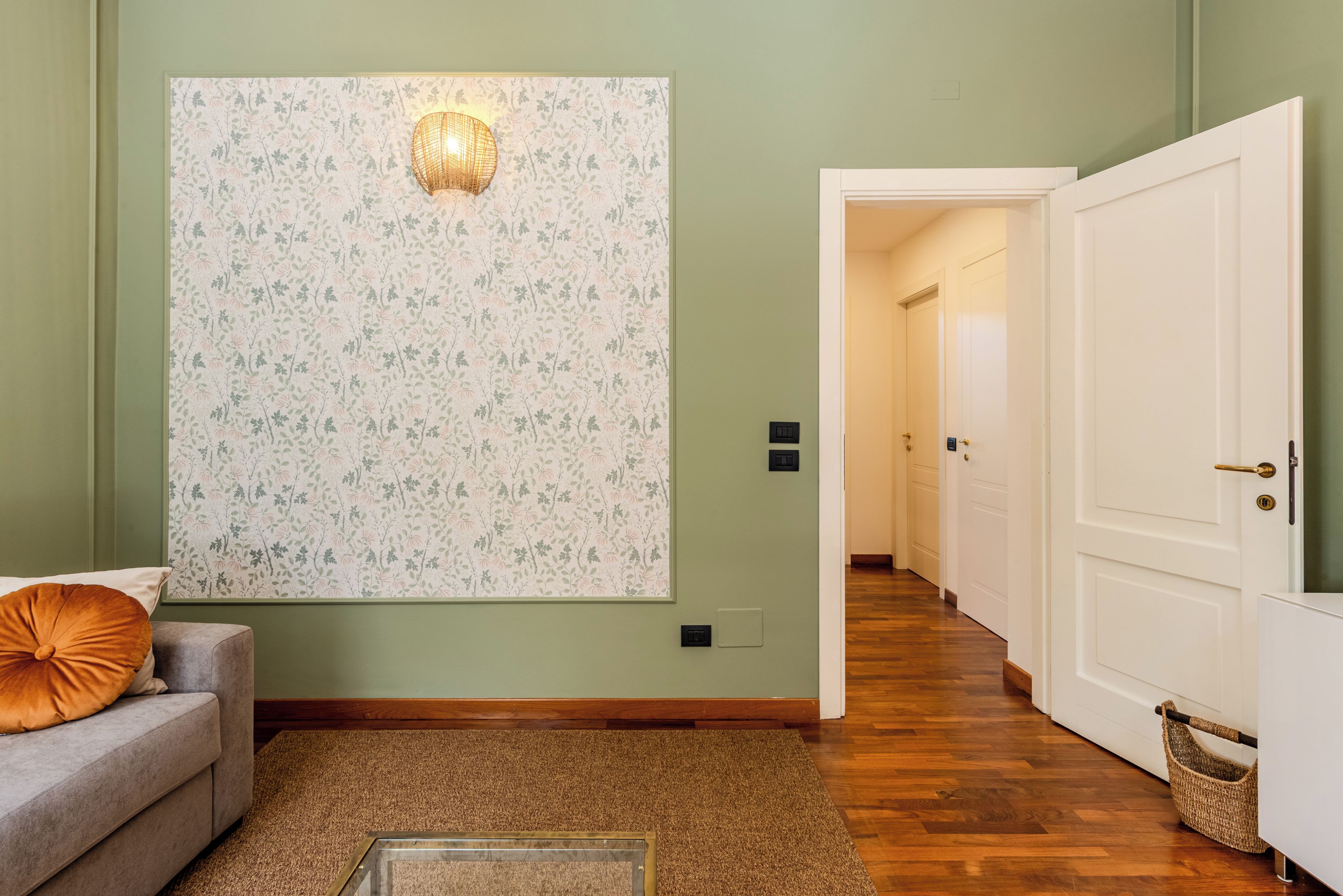 A hallway with a patterned wall, a sofa with a cushion, and a wooden floor.