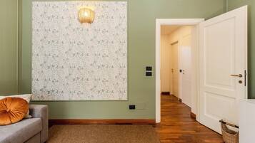 A hallway with a patterned wall, a sofa with a cushion, and a wooden floor.