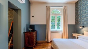 Un dormitorio con cómoda de madera, una cama, una ventana con cortinas y una pared con estampado floral.