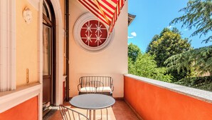 Un balcón con una mesa redonda y dos sillas, un toldo a rayas rojas y blancas, y una ventana circular con un diseño blanco.