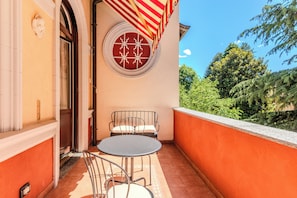 A balcony with a round table and two chairs, a red and white striped awning, and a circular window with a white pattern. - Vrbo Property (Mozzate)