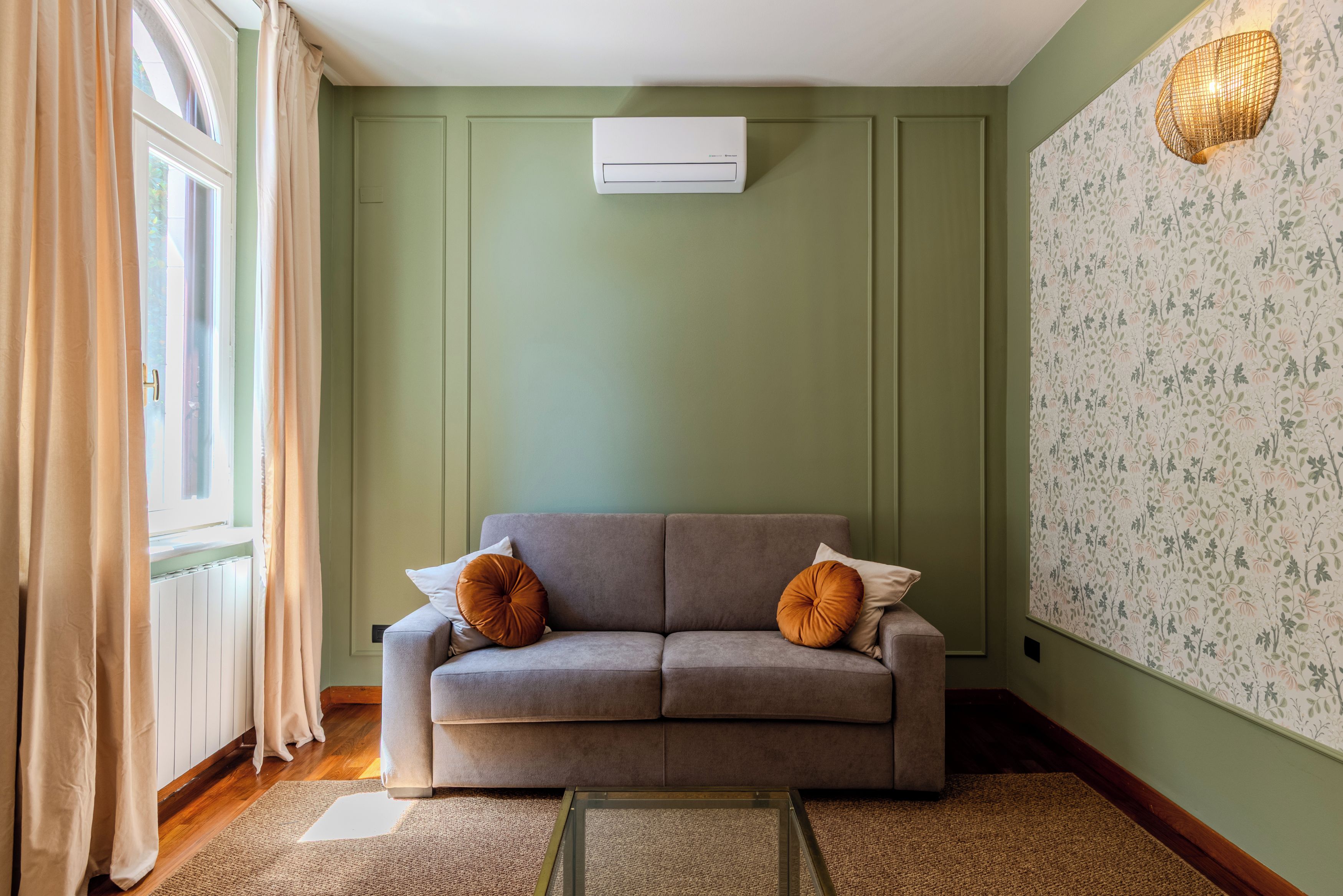 Quarto com sofá, radiador, janela com cortinas e parede com papel de parede floral.
