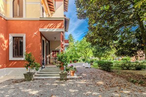 A building with a red facade, a covered entrance, and a gravel pathway leading to a seating area. - Villa dei Ricordi_Mozzate_Apartment 3 (Mozzate)