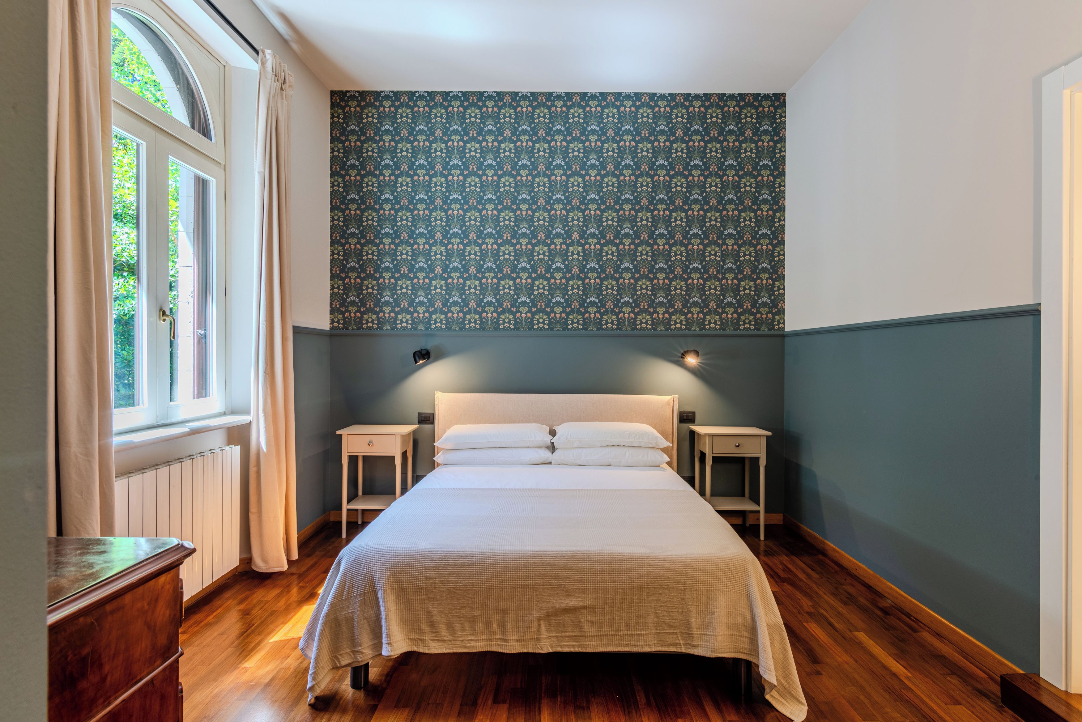 Quarto com uma cama grande, duas mesas de cabeceira, cômoda e uma janela com cortinas.