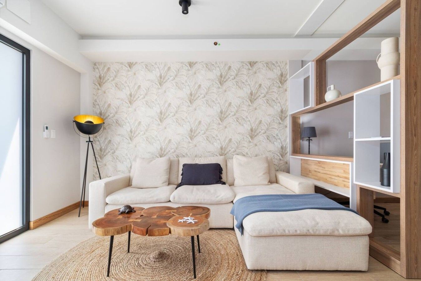 A modern living room with a sofa, coffee table, and ottoman. There is a floor lamp and a bookshelf.
