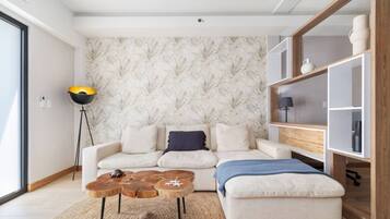A modern living room with a sofa, coffee table, and ottoman. There is a floor lamp and a bookshelf.