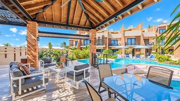 A covered outdoor area with a pool, lounge chairs, and a glass table.