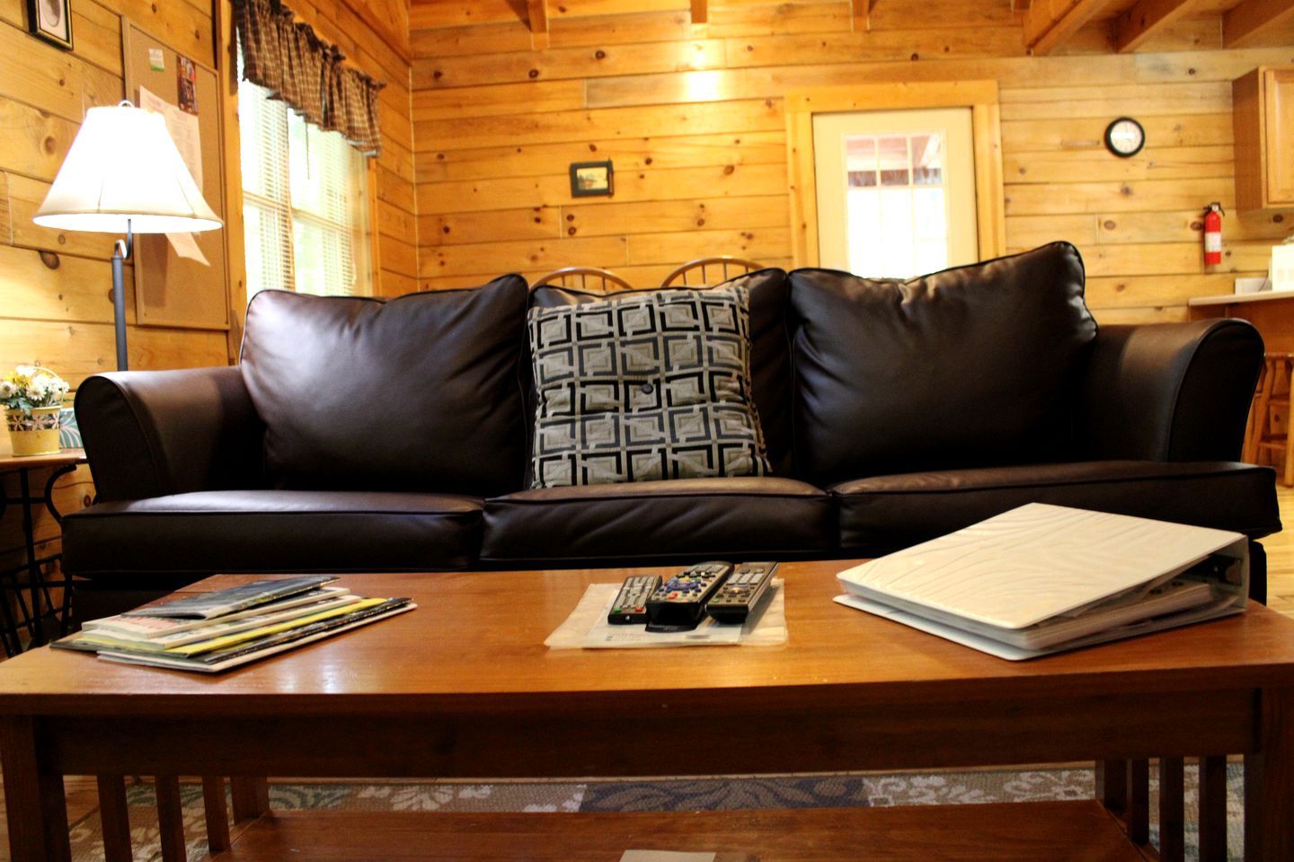 Ein Holzinterieur mit einem Ledersofa, einer Lampe, einem Tisch mit Zeitschriften und Fernbedienungen sowie einem Feuerlöscher.
