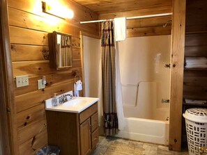 Bagno di una casetta di legno con lavandino, specchio e doccia.