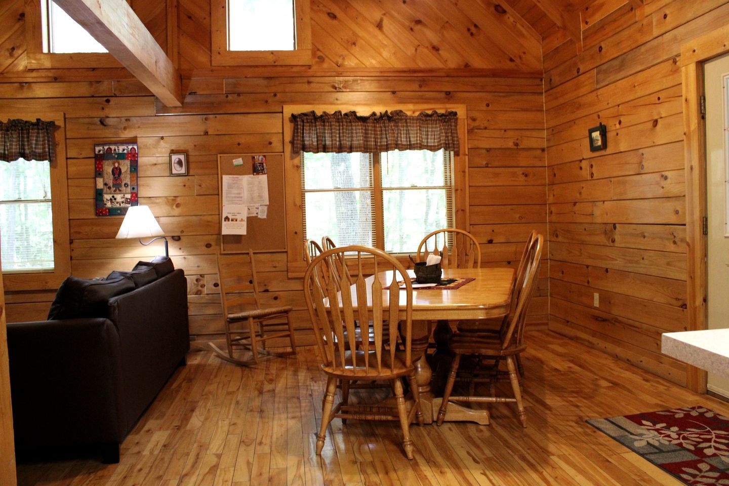L’intérieur d’un chalet accueillant, avec une table à manger en bois, des chaises, un canapé et une fenêtre agrémentée de rideaux.