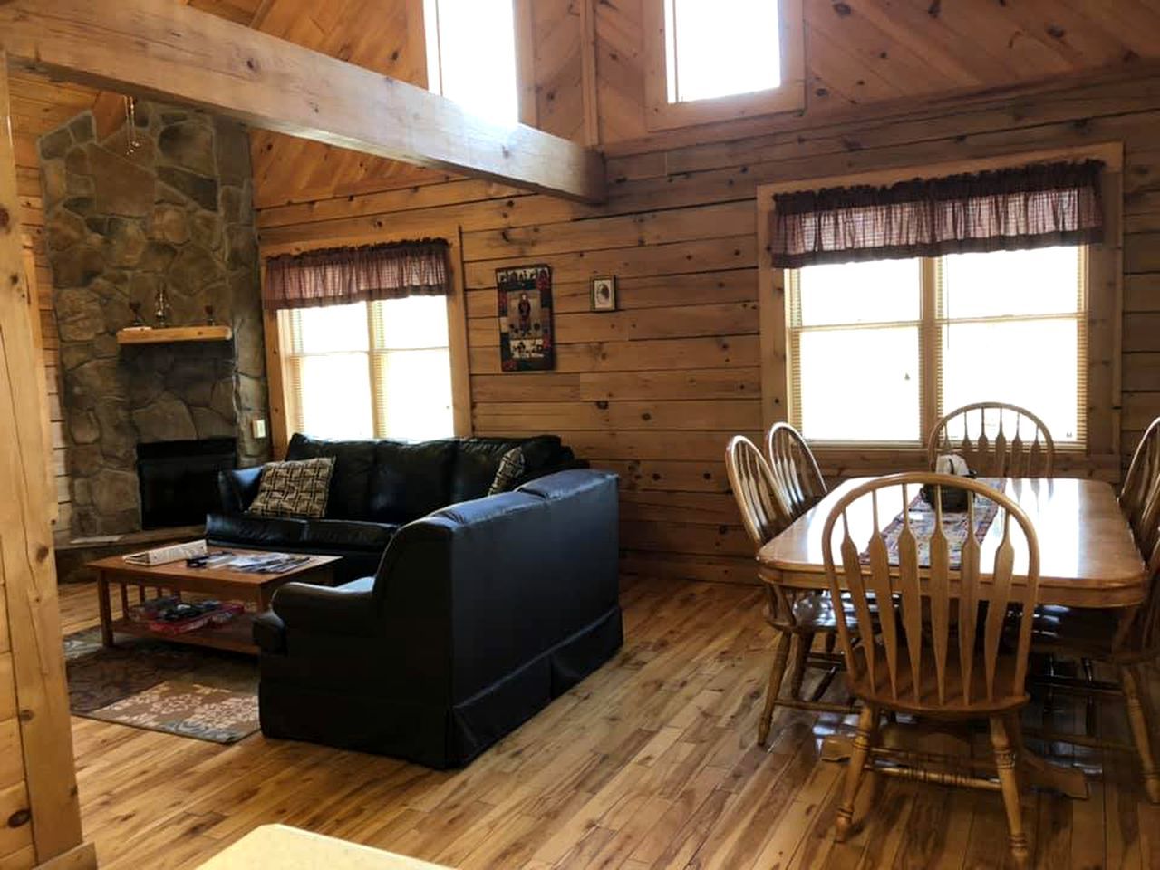 Un intérieur en bois avec une cheminée en pierre, un canapé, une table à manger avec des chaises et une fenêtre avec des rideaux.
