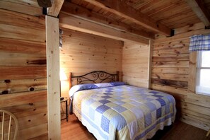 A wooden cabin room with a bed, a nightstand, and a window with curtains. - Spacious Cabin Rental with a Hot Tub near the Gauley River in West Virginia (Hico)
