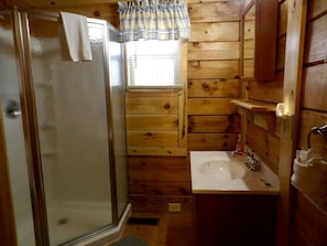 Ein Badezimmer einer Holzhütte mit Dusche, Waschbecken und Fenster.