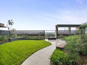 A modern outdoor space with a curved pathway, a grassy area, and a covered seating area. - Skyline 1-bed Apartment Near Melbourne CBD (Melbourne)