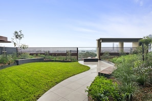 A modern outdoor space with a curved pathway, a grassy lawn, and a view of the cityscape. - Skyline 1-bed Apartment Near Melbourne CBD (Melbourne)